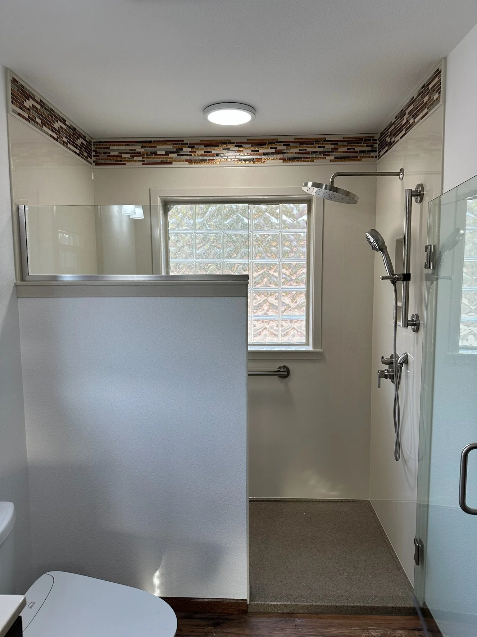 A bathroom with a glass block window, a walk-in shower with two shower heads, a grab bar, and a partial wall.