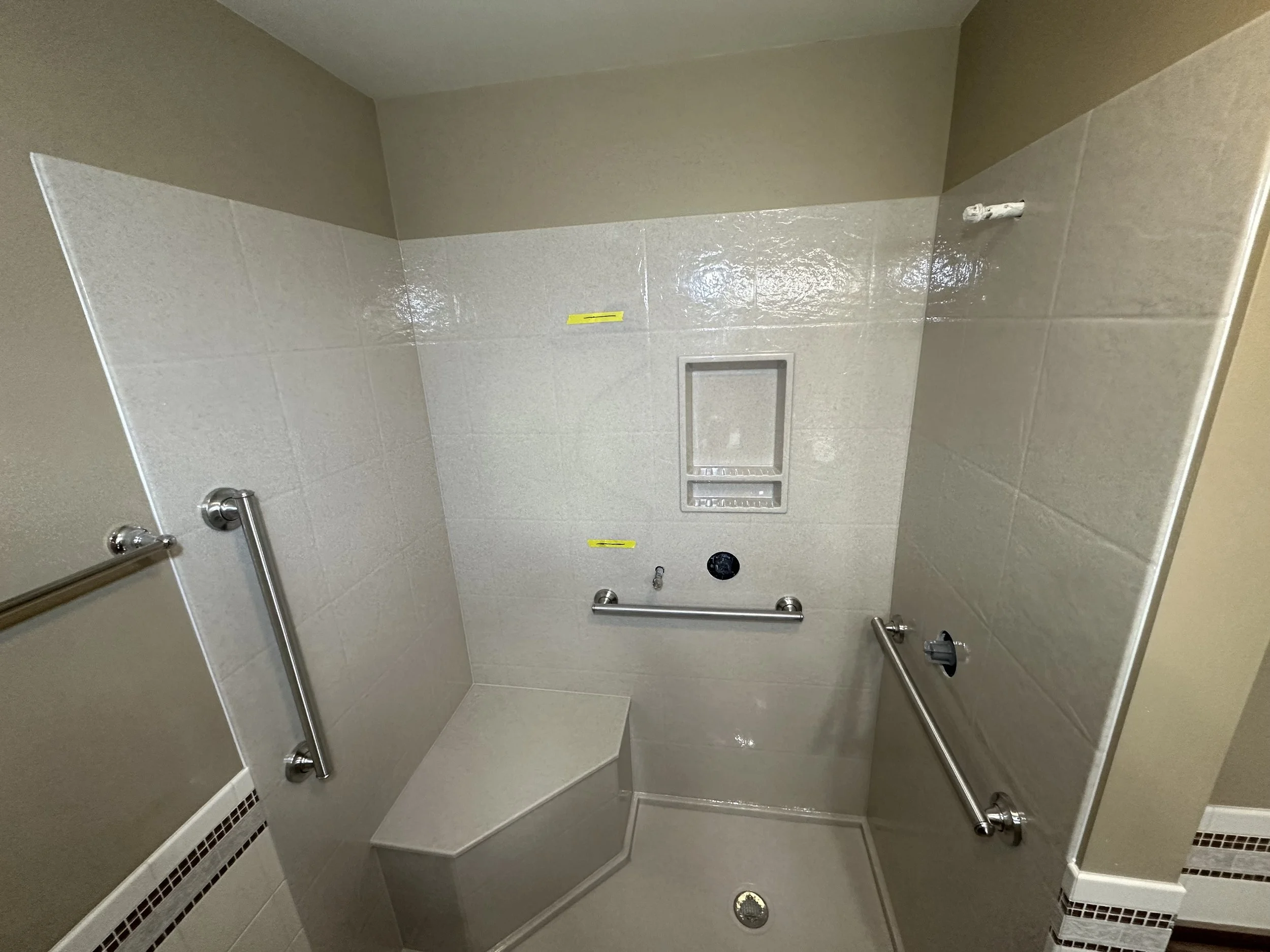 Inside a shower stall with grab bars, a built-in bench, and a small access panel on the wall.