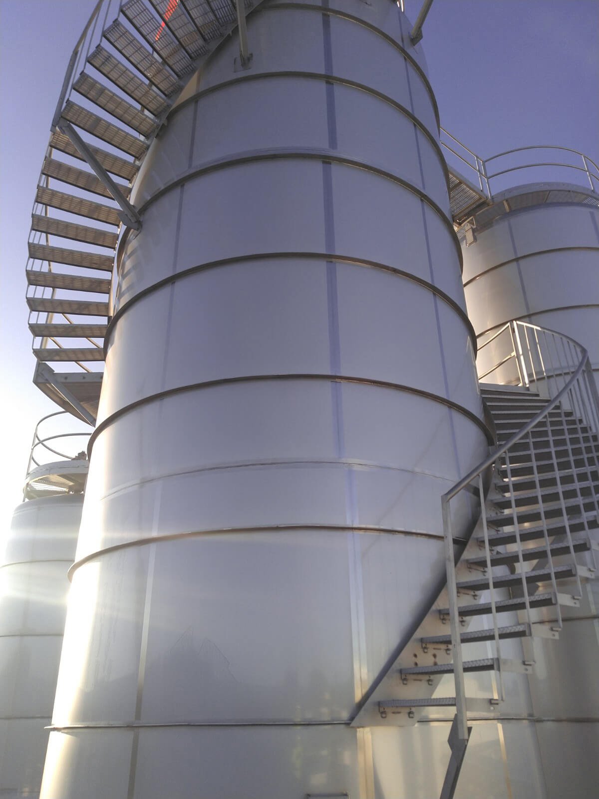 Large, cylindrical white industrial storage tanks with metal stairs and railings.