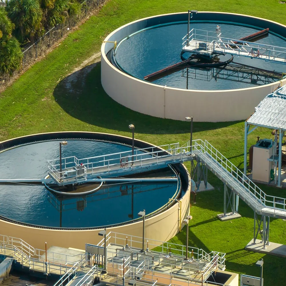 Aerial view of a water treatment plant with large circular clarifiers, metal walkways, and green grassy areas.