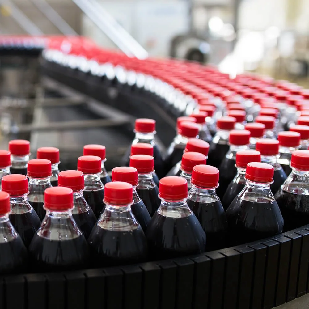 Bottles of soda with red caps on a production line in a factory.