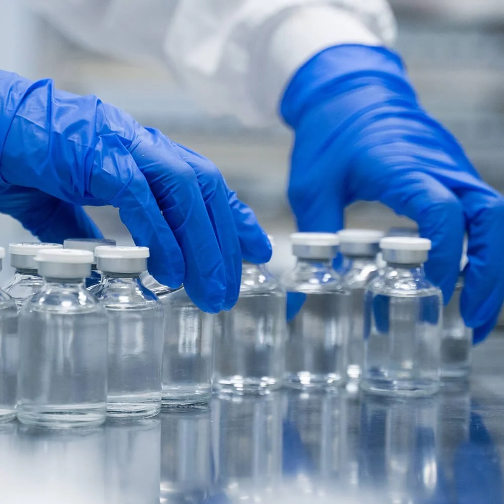 Person wearing blue gloves handling small glass vials in a laboratory setting.