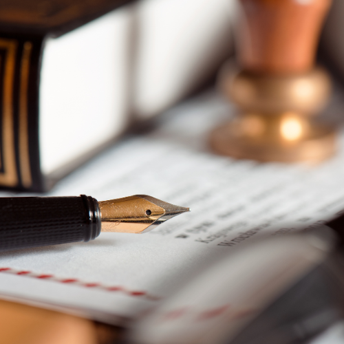 Close-up of a fountain pen resting on a lined notebook with a blurred plant and book in the background.