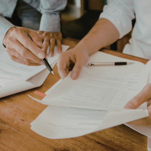 People reviewing and signing documents on a wooden table, with papers and pens.