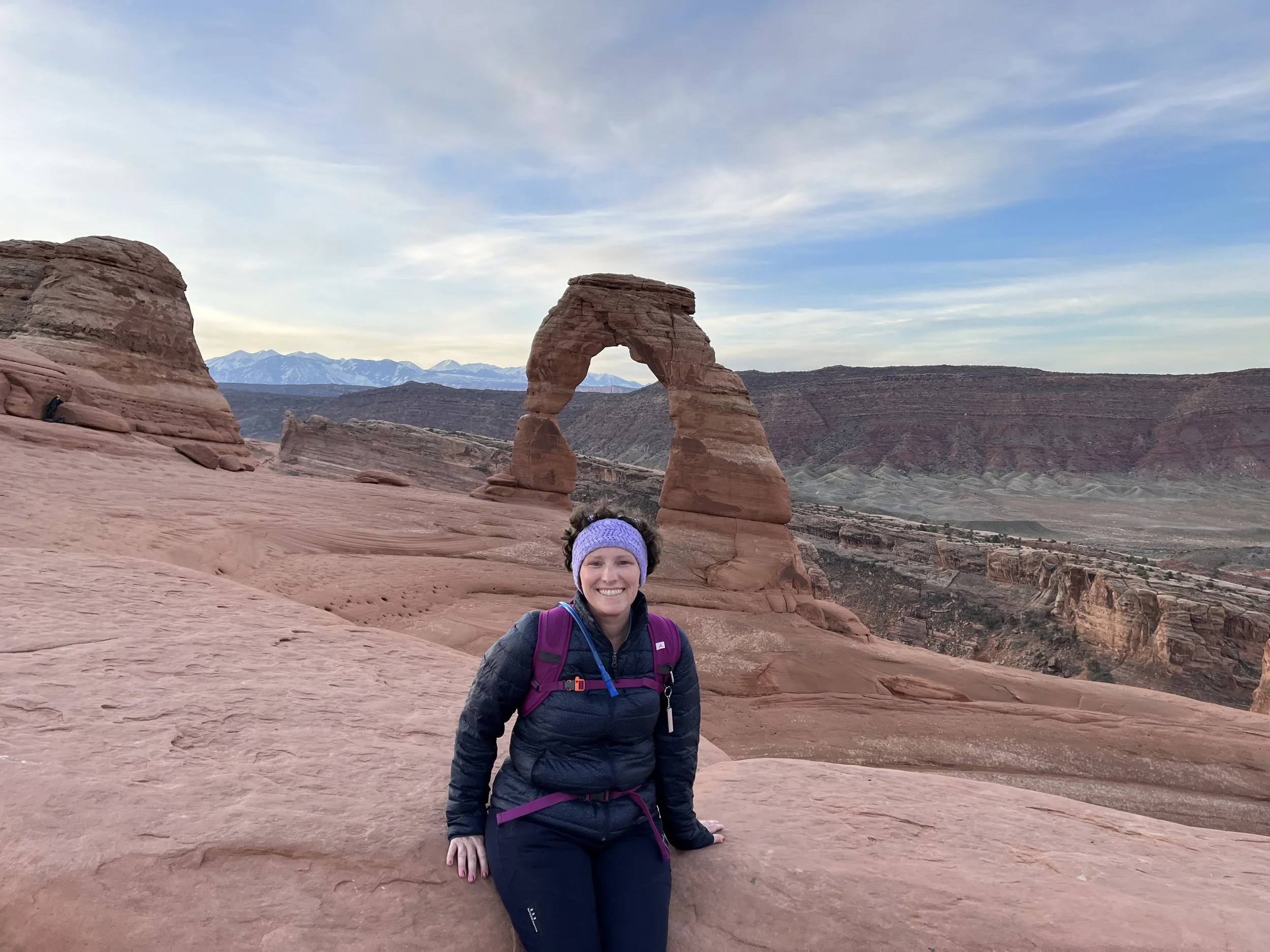 Amanda at Arches National Park, smiling on red sandstone with Delicate Arch in the background