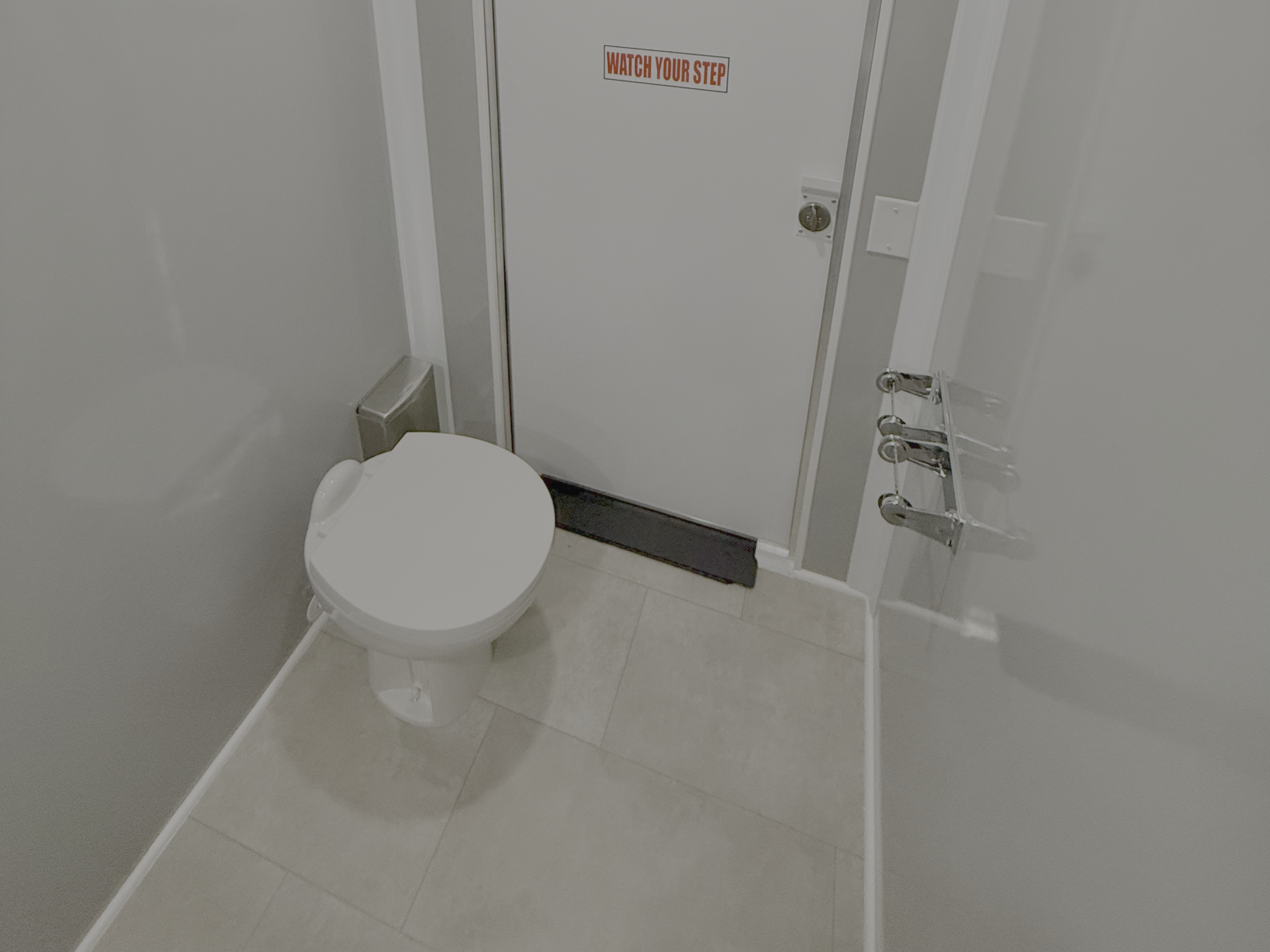 Luxury restroom trailer with bathroom with a white toilet, a door with a lock, and a sign that says 'WATCH YOUR STEP.'