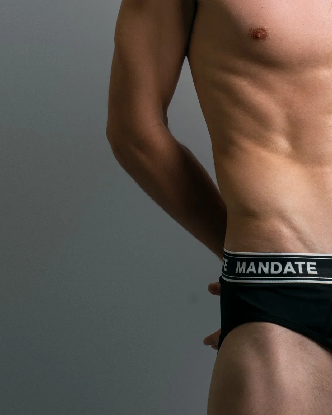 Side view of Mandate black low-rise swim brief with branded waistband on model