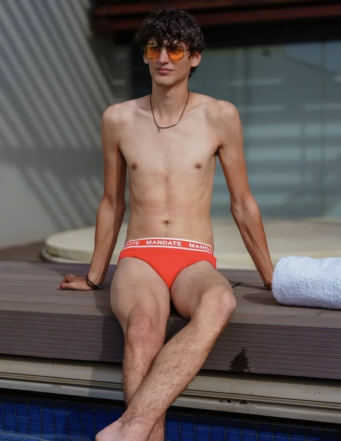 Young boy sitting on pool deck in red swimwear 
