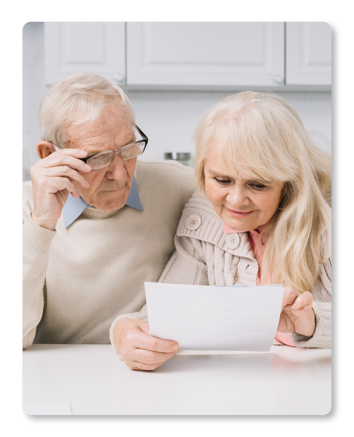 Un couple de personnes âgées regarde un document ou une lettre ensemble à la maison autour d'une table.