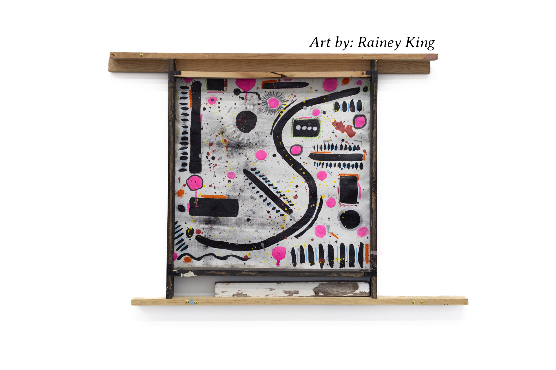 Abstract mixed-media artwork by Rainey King, featuring black, pink, orange, and yellow shapes and splatters on a gray background, framed with wood and metal.