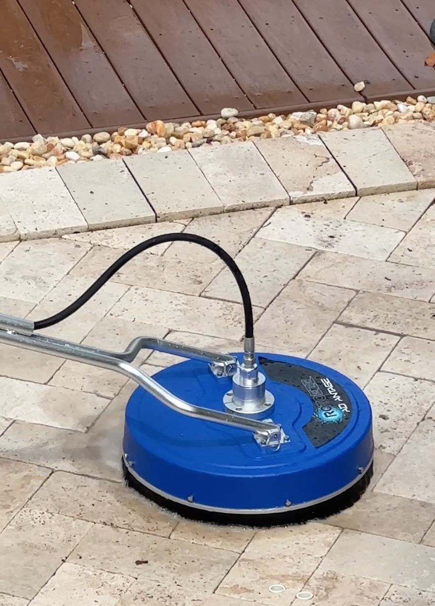 A blue floor polishing machine on a tiled surface, surrounded by a wood and gravel border in an outdoor area.