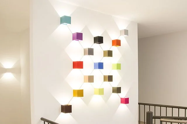 Moderne Wandbeleuchtung mit bunten quadratischen Lampen in verschiedenen Farben an einer weißen Wand.