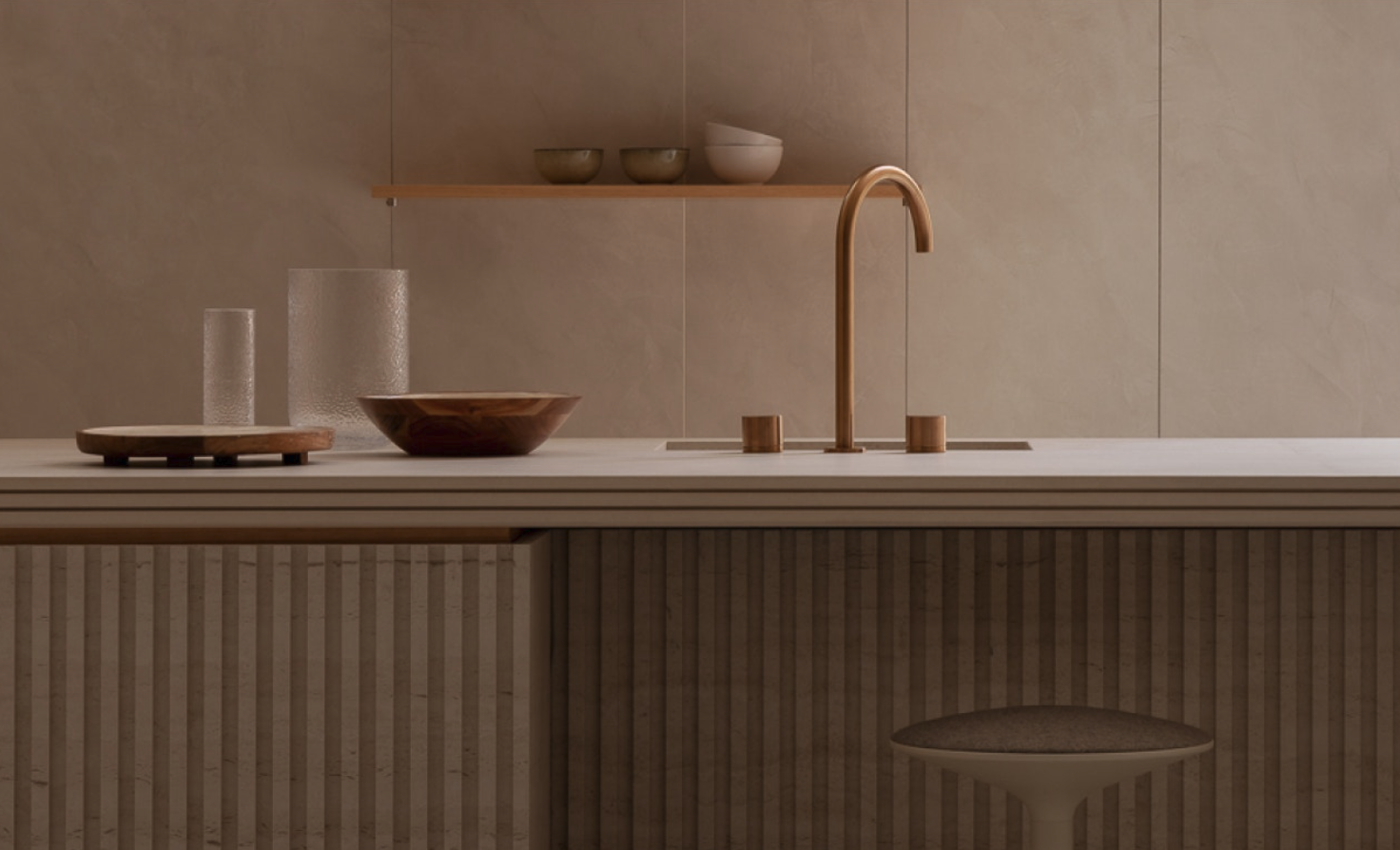 Minimalist kitchen with beige tiled wall, wooden floating shelf with bowls, a brass faucet, and a wooden countertop with a bowl and glasses.