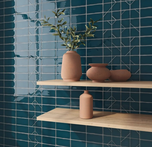 Two wooden shelves on a blue tiled wall, with three beige vases containing a leafy plant and decorative objects.