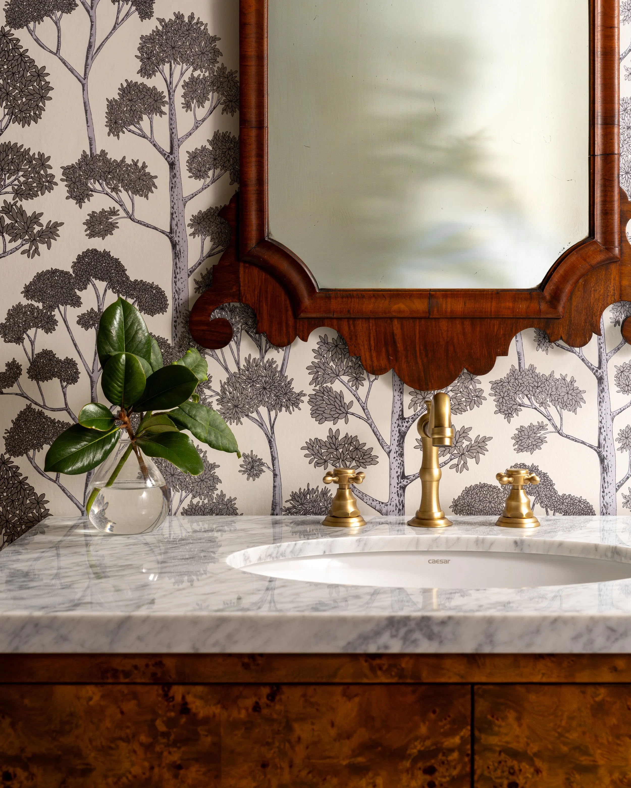 Bainbridge Island luxury powder room with burl wood vanity, marble countertop, brass fixtures, and scenic tree pattern wallpaper.