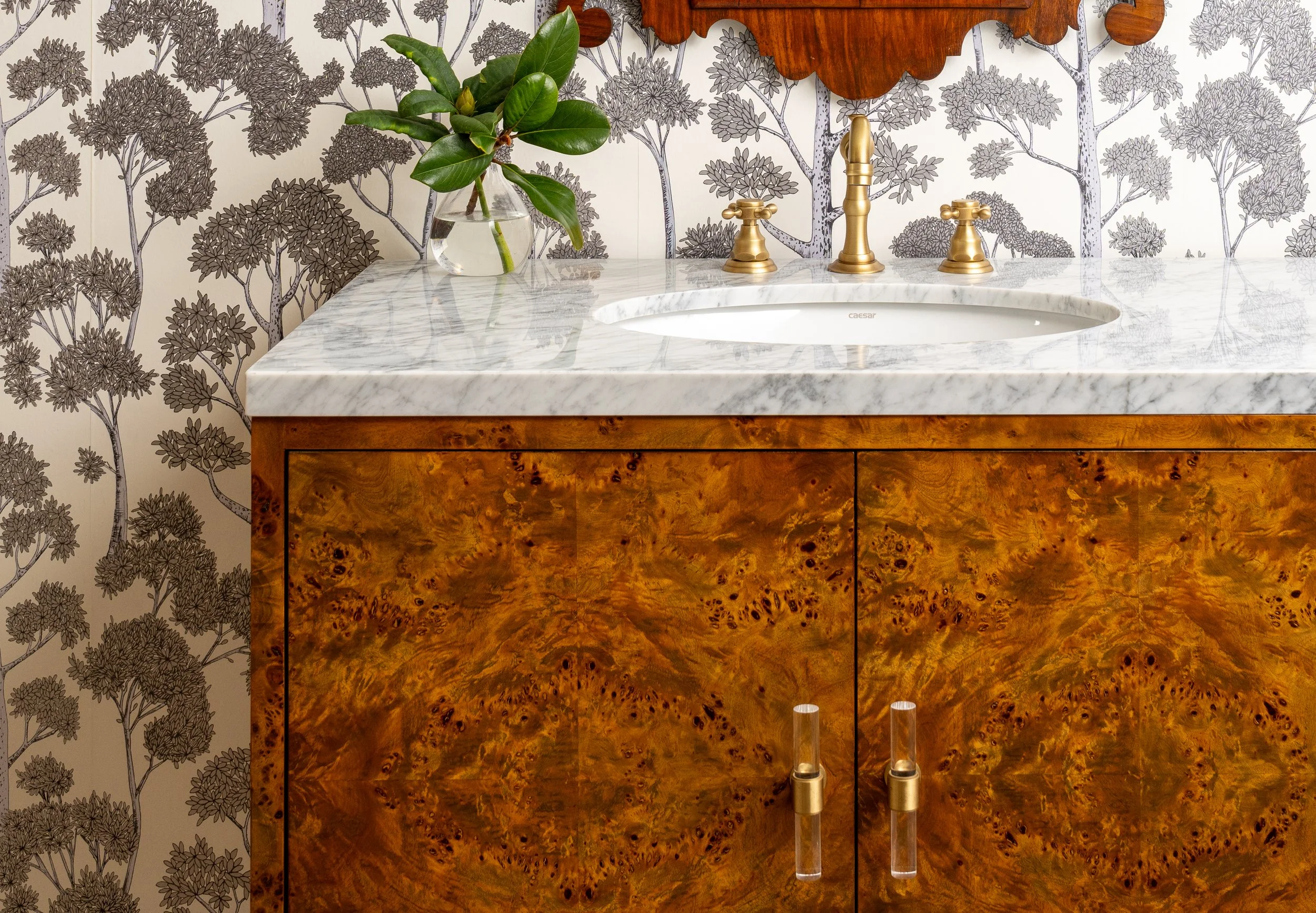 Burl wood vanity cabinet with white marble countertop and brass fixtures set against monochrome forest wallpaper by Emily Barrows Photography.