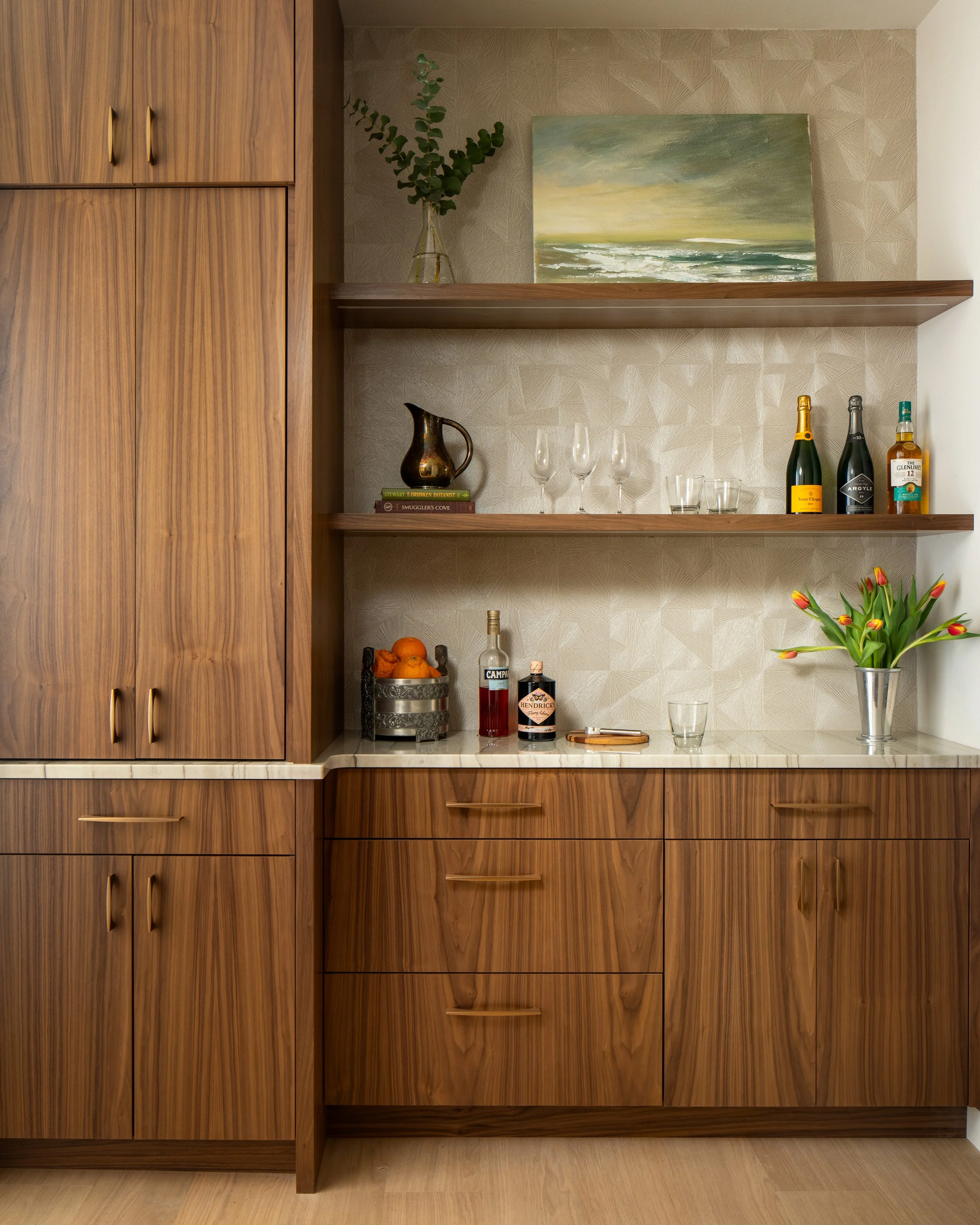 Bainbridge Island modern home bar with custom walnut cabinetry, marble countertop, textured geometric wallpaper, and floating wood shelves.	