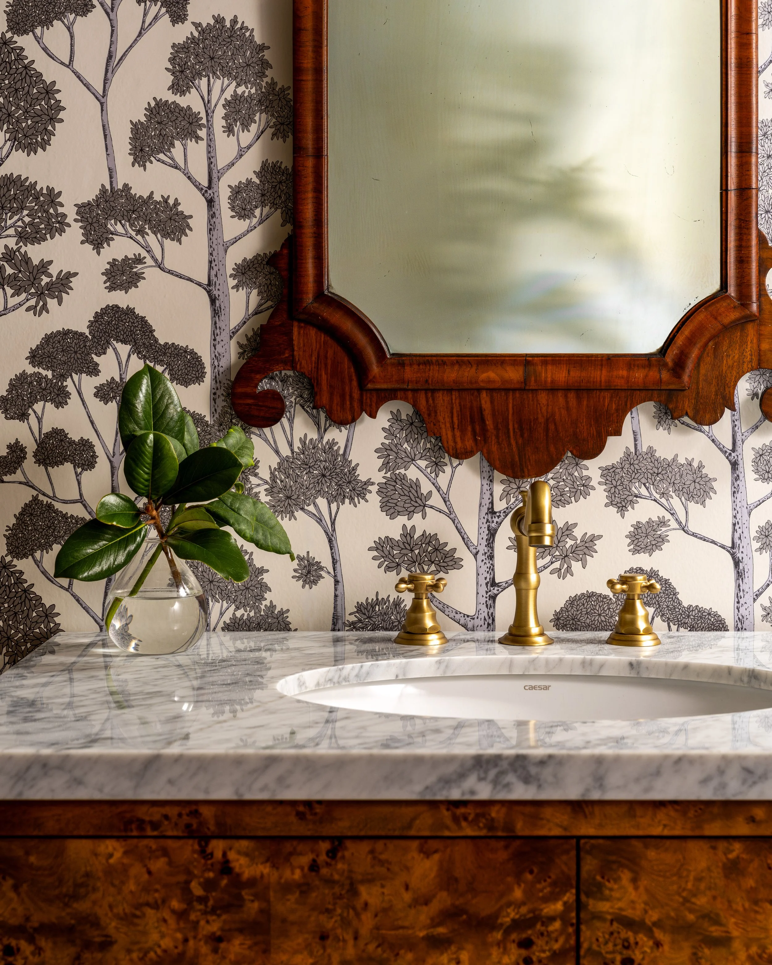 Bainbridge Island luxury powder room with burl wood vanity, marble countertop, brass fixtures, and scenic tree pattern wallpaper.