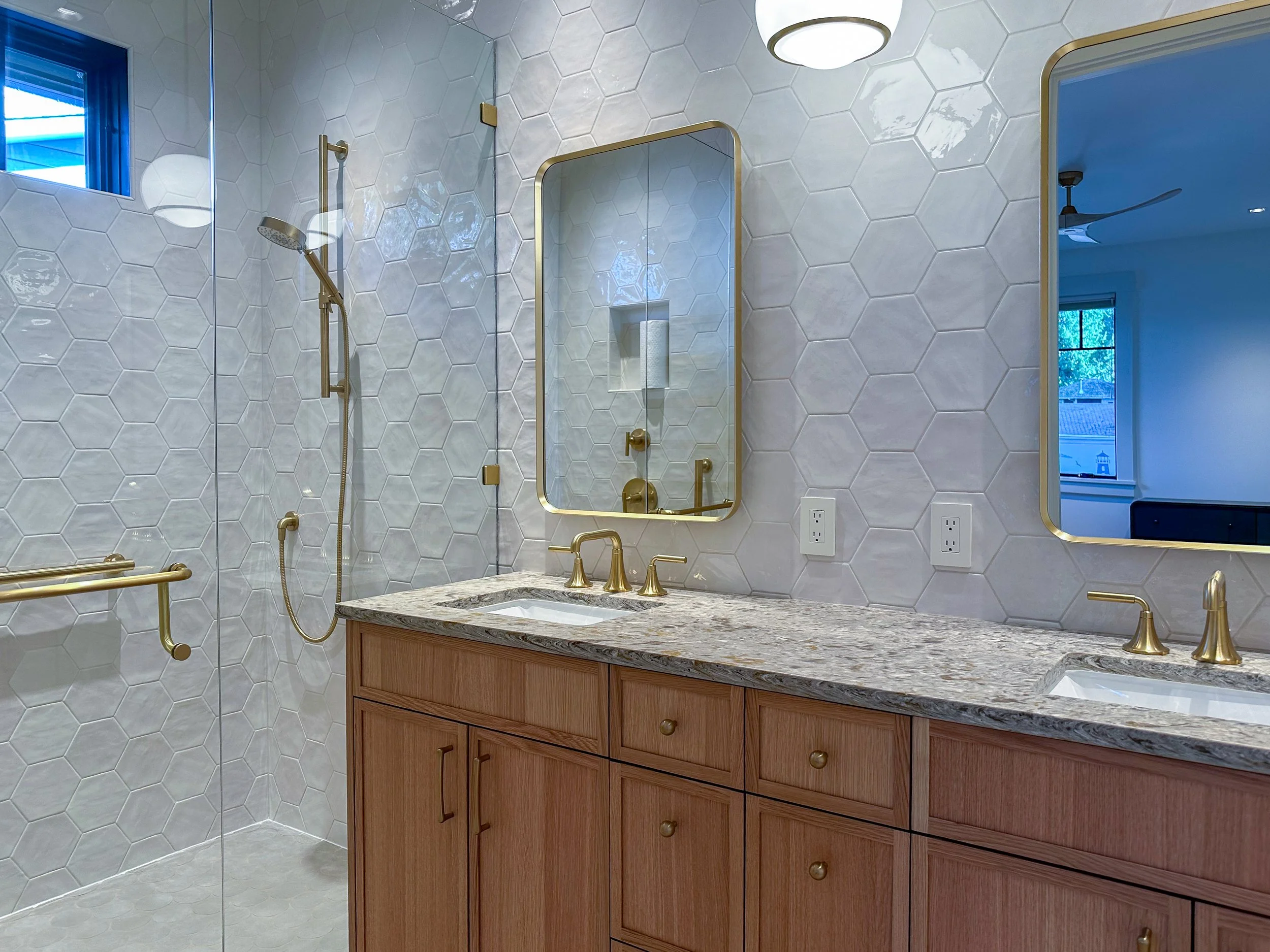 Bathroom with a double vanity, gold fixtures, and a walk-in shower with honeycomb tiles.