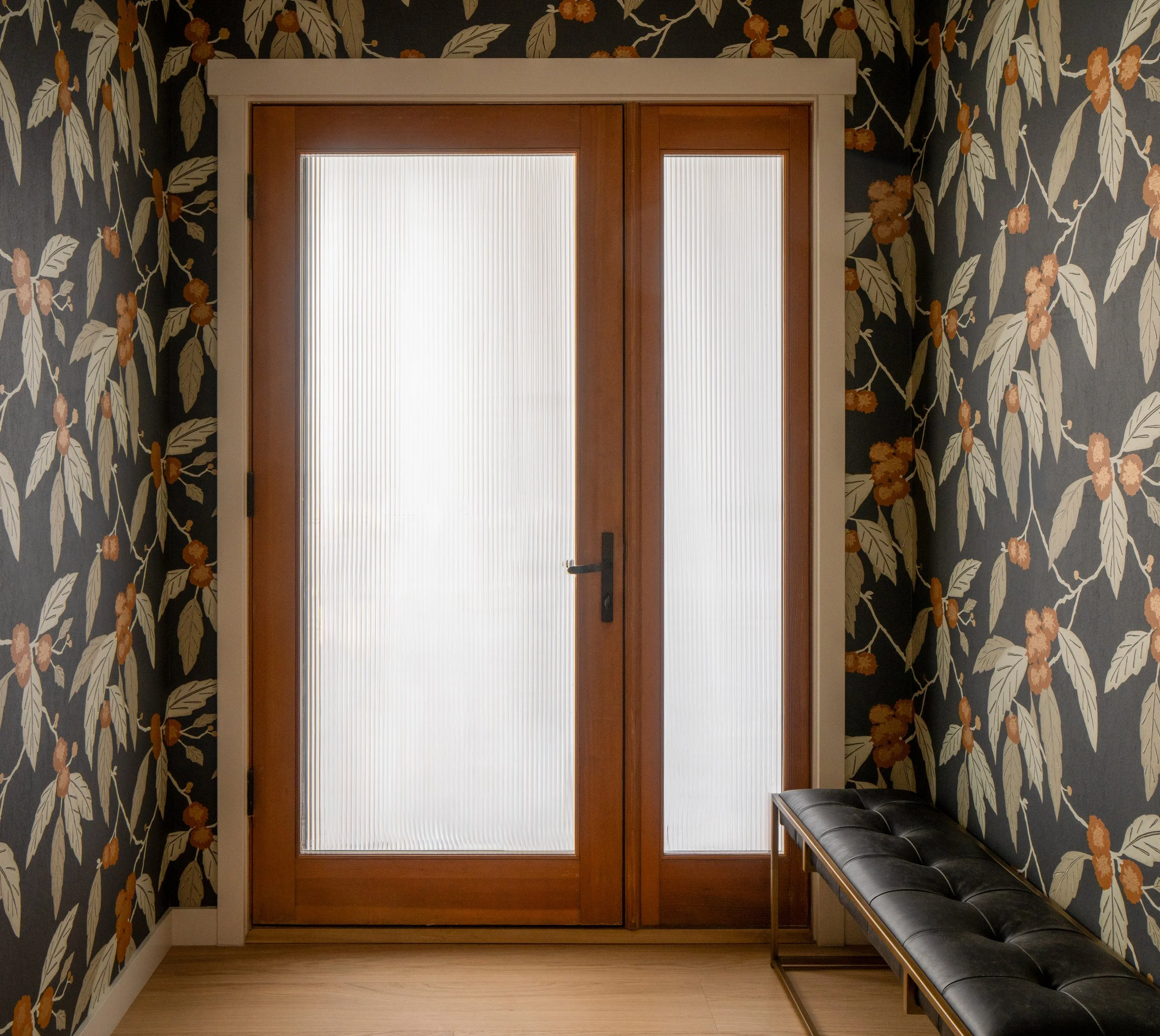 Bainbridge Island entryway featuring dark botanical pattern wallpaper, fluted glass door inserts, and a black tufted leather bench.
