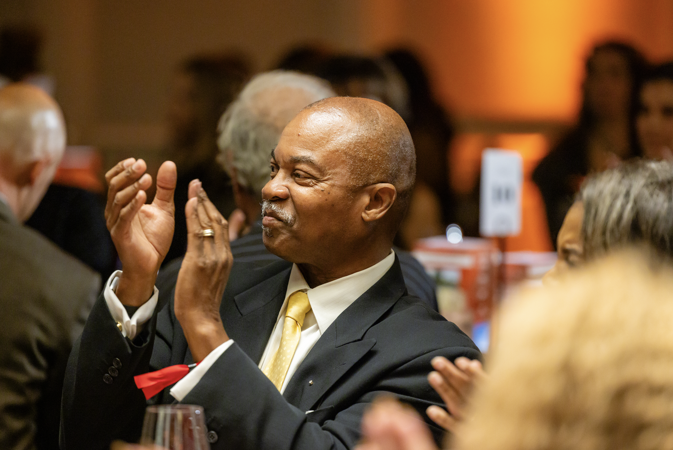 A man in a suit and yellow tie engaging in conversation at a social event.