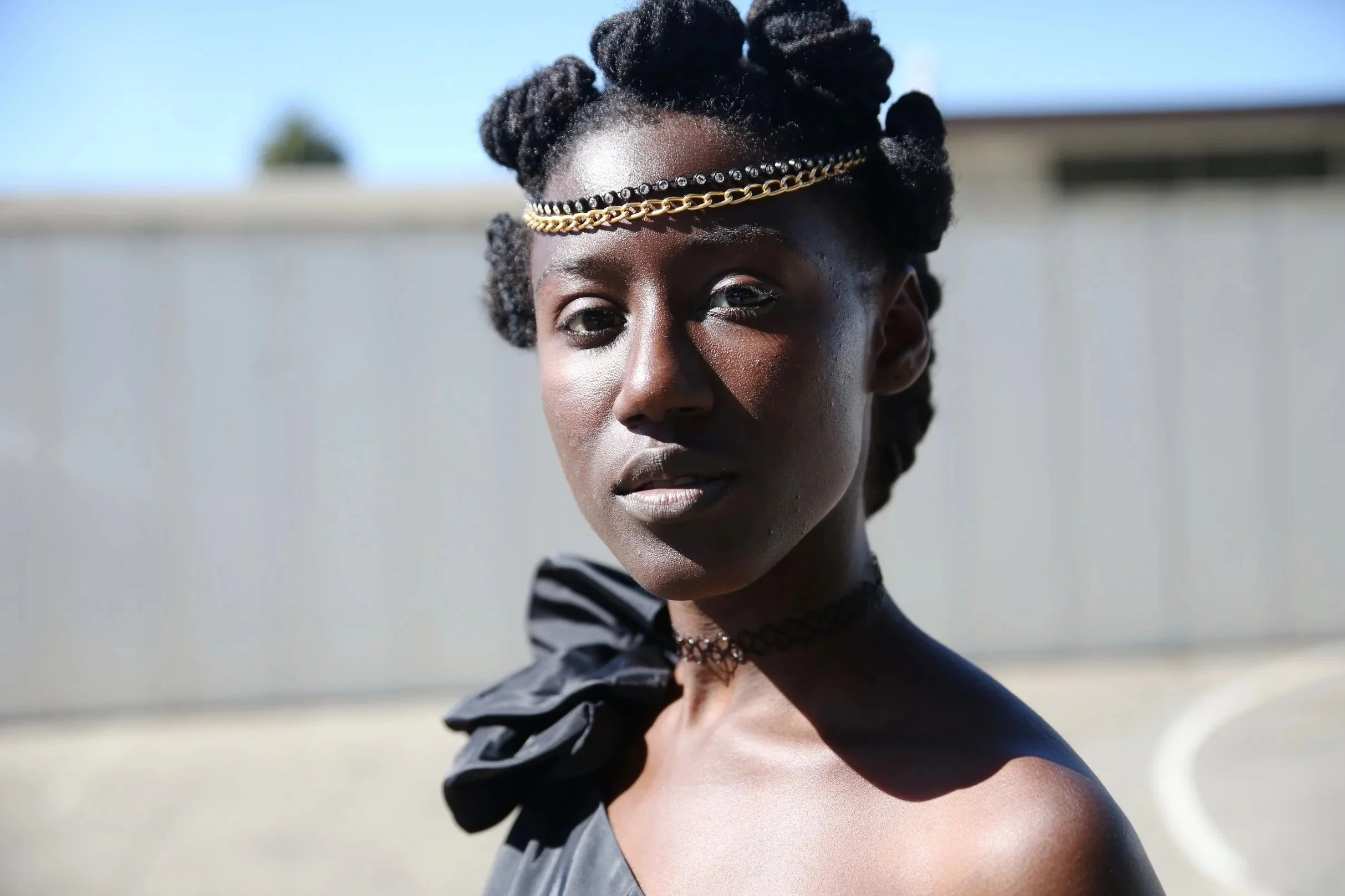 Close-up of a woman with styled dreadlocked hair, wearing jewelry and a striped top, outdoors against a blurred background.