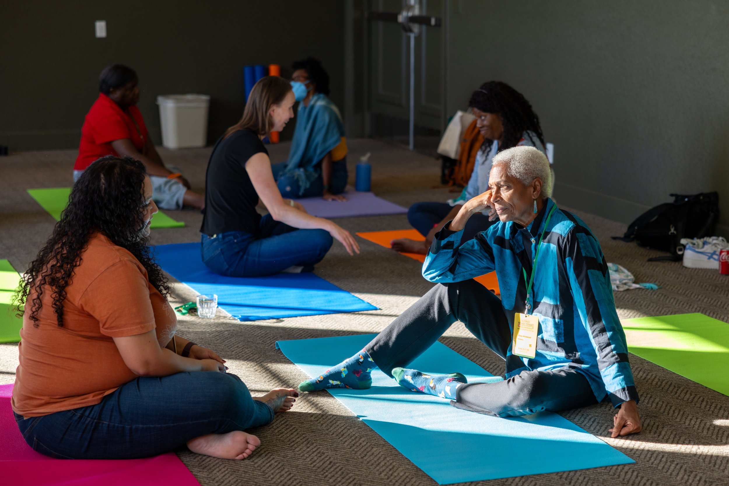 Group of diverse individuals practicing yoga and meditation on colorful mats in a well-lit room.