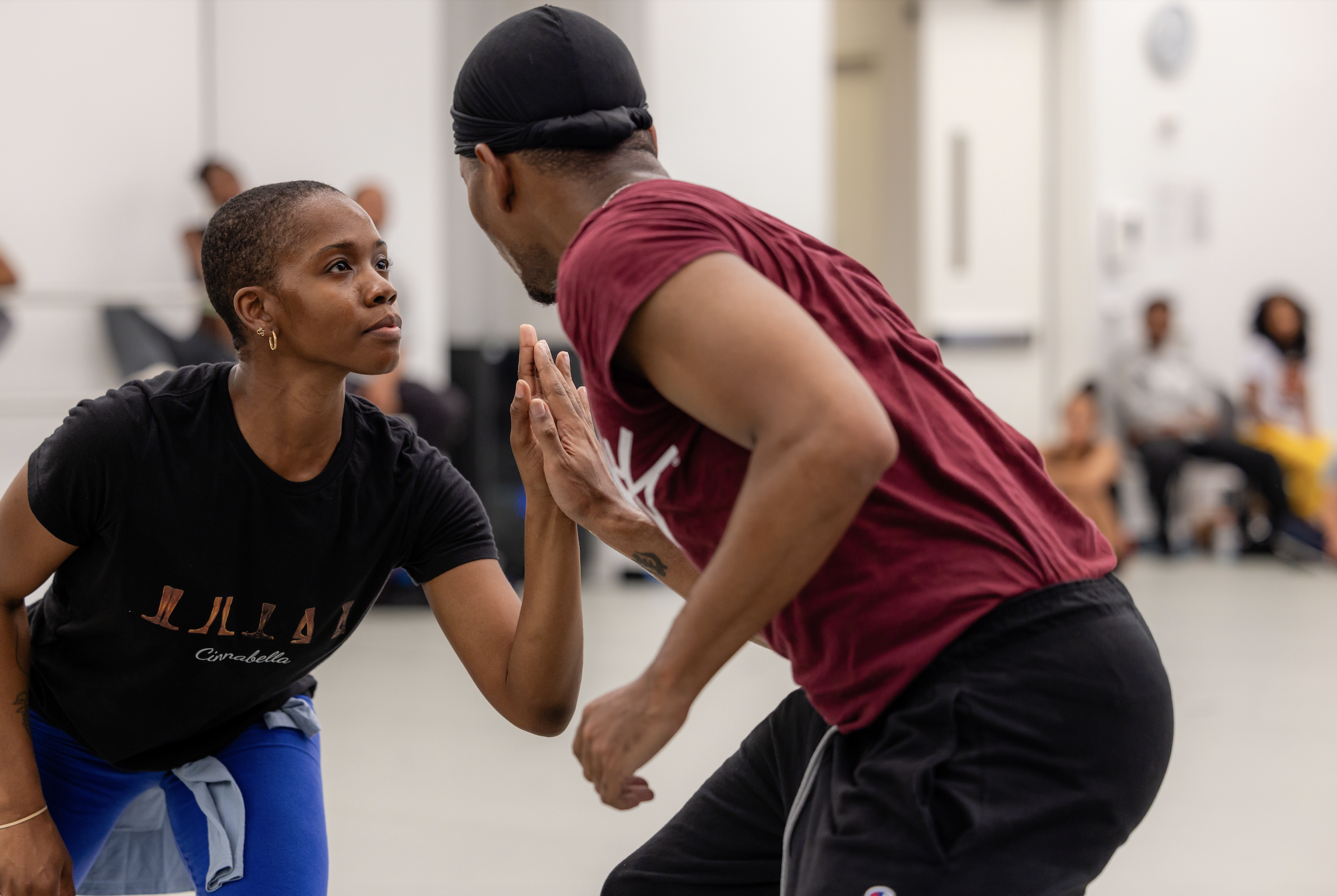 A woman and a man practicing a martial arts technique in a group class, with other participants blurred in the background.