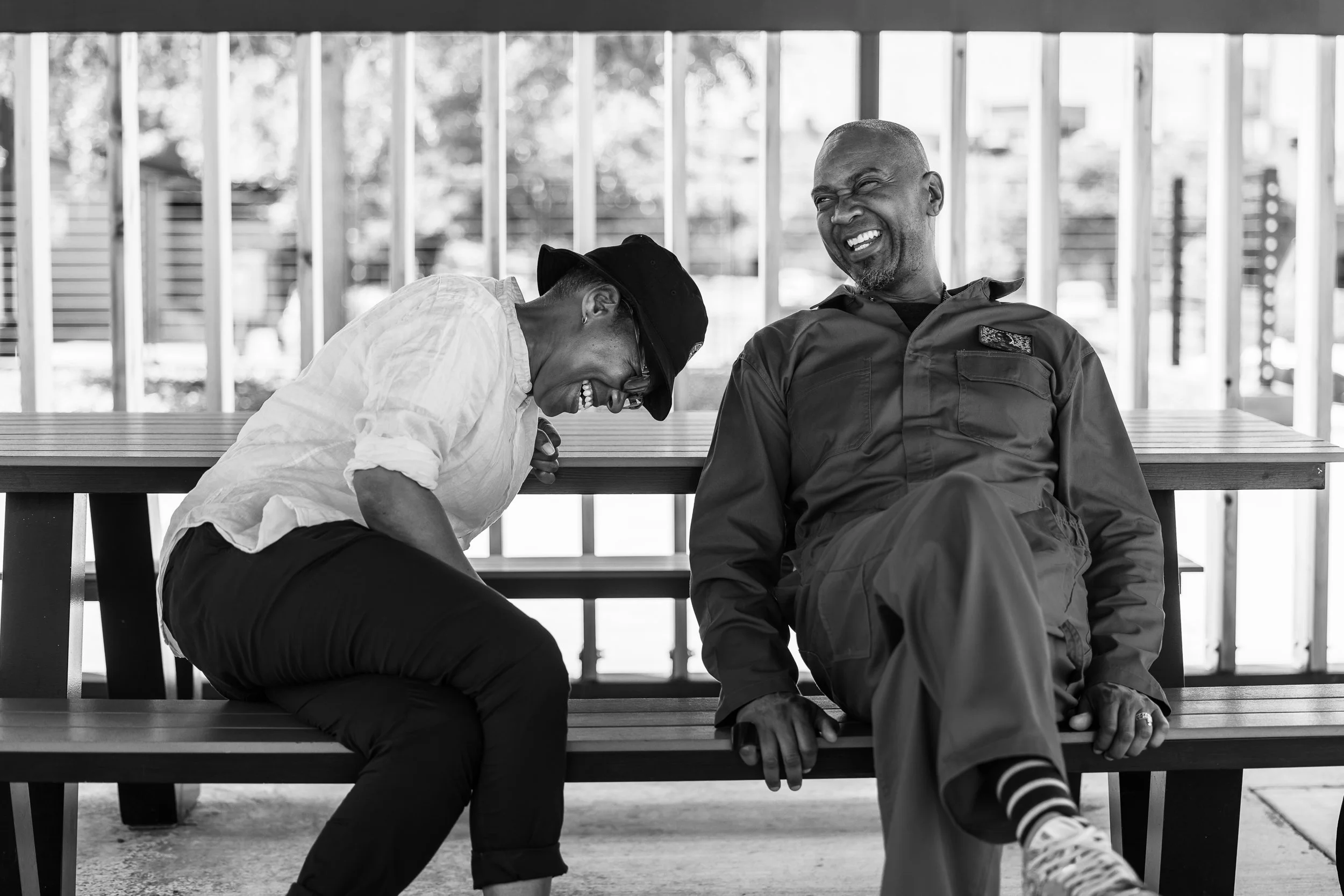 A man and woman are sitting on a bench outdoors, laughing and sharing a joyful moment.