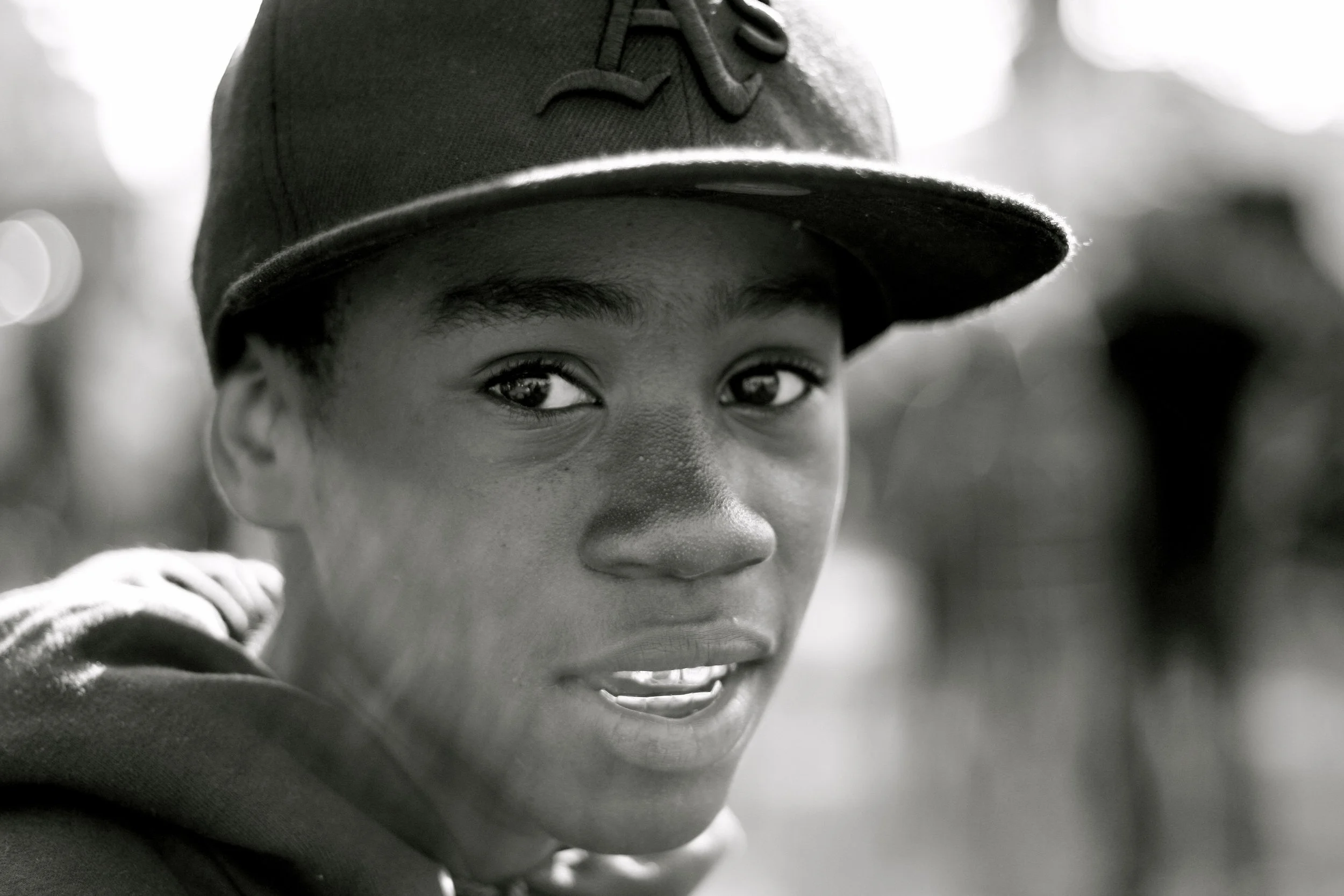 Close-up of a young child's face wearing a baseball cap, showing a peek of a bright smile.