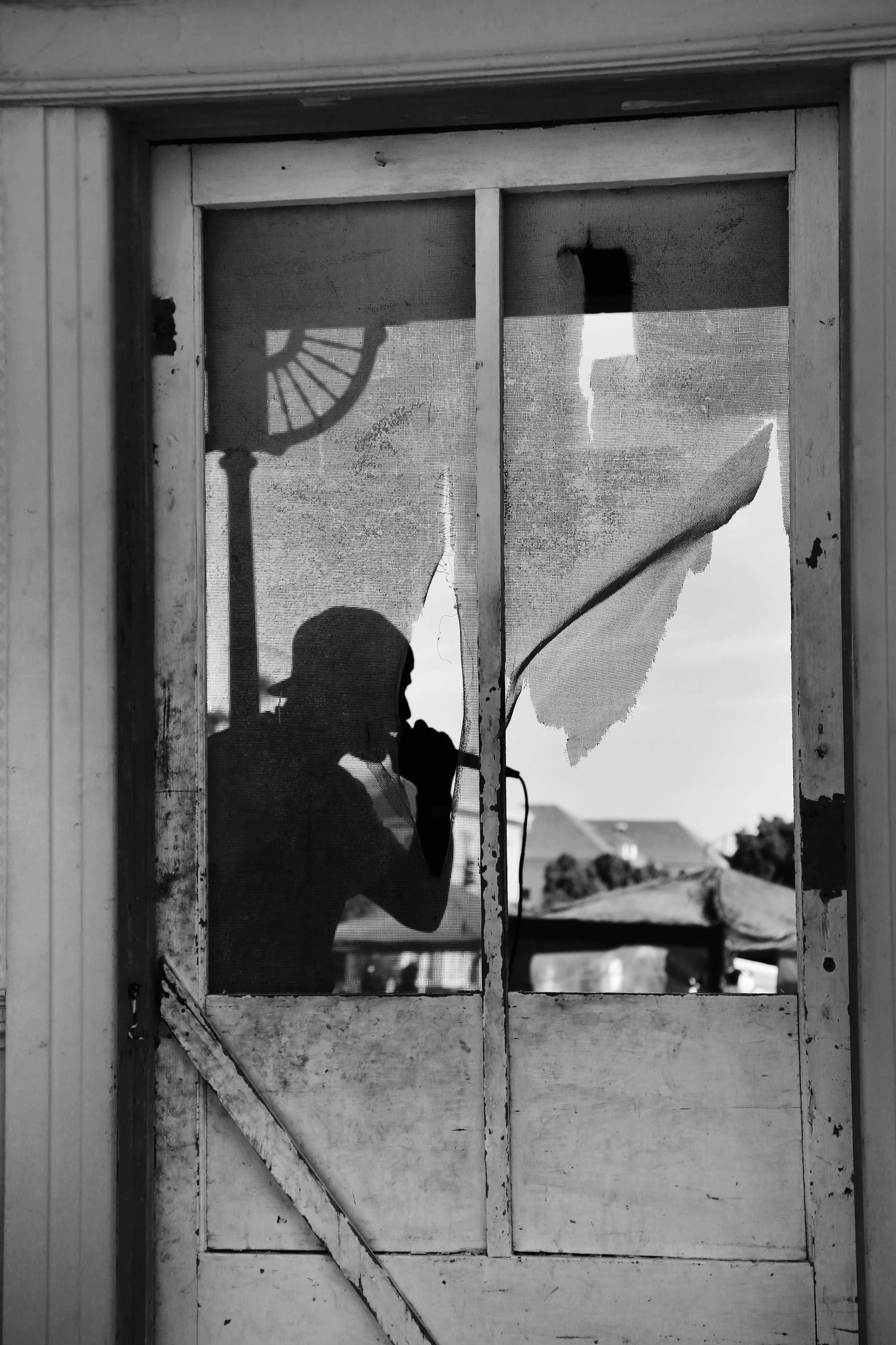 Person taking a photo of their reflection in a window with a torn or damaged screen, with a silhouette of a statue or monument visible outside.