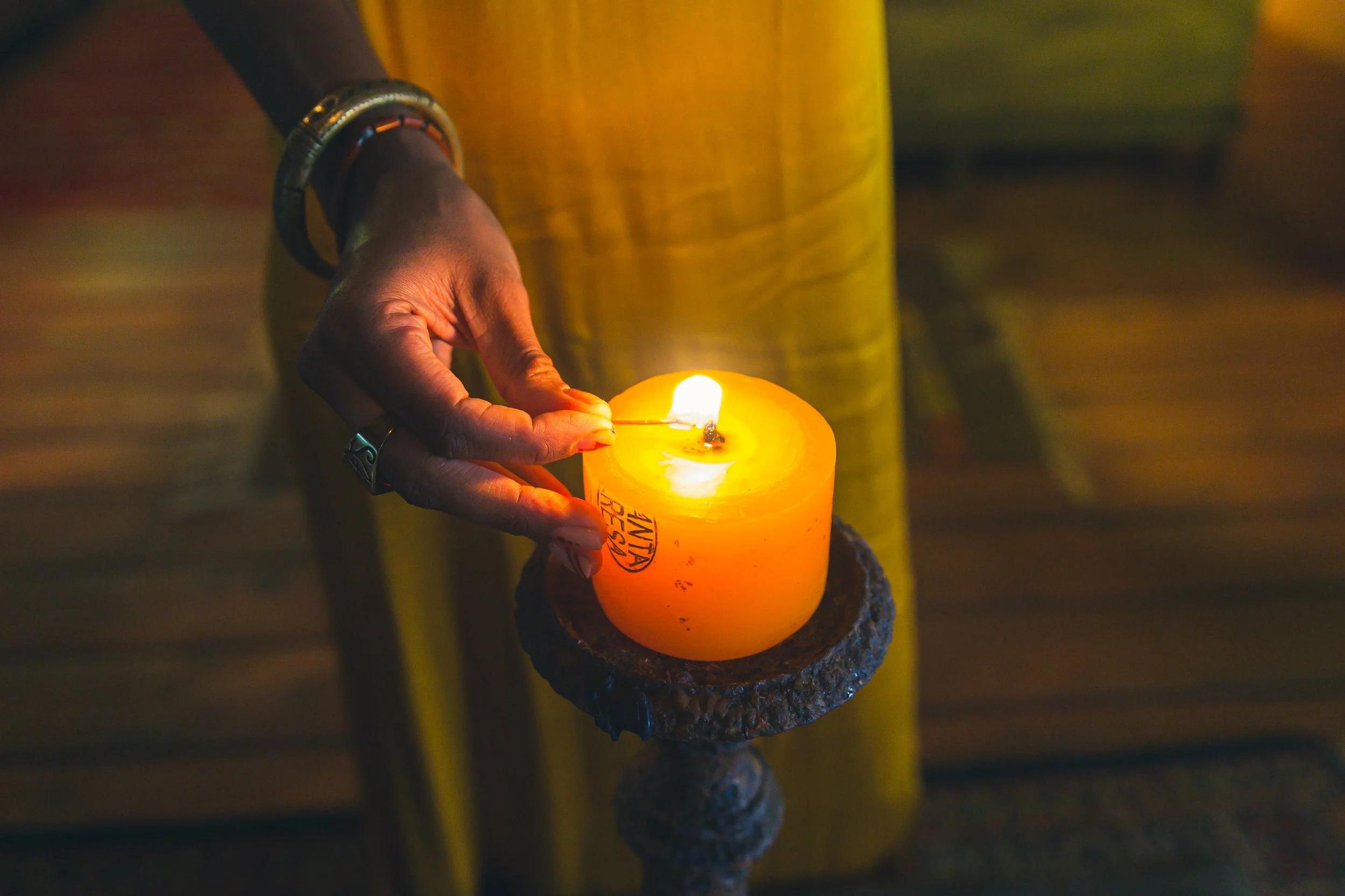 A person holding a lit candle with yellow and orange colors in a dark setting.