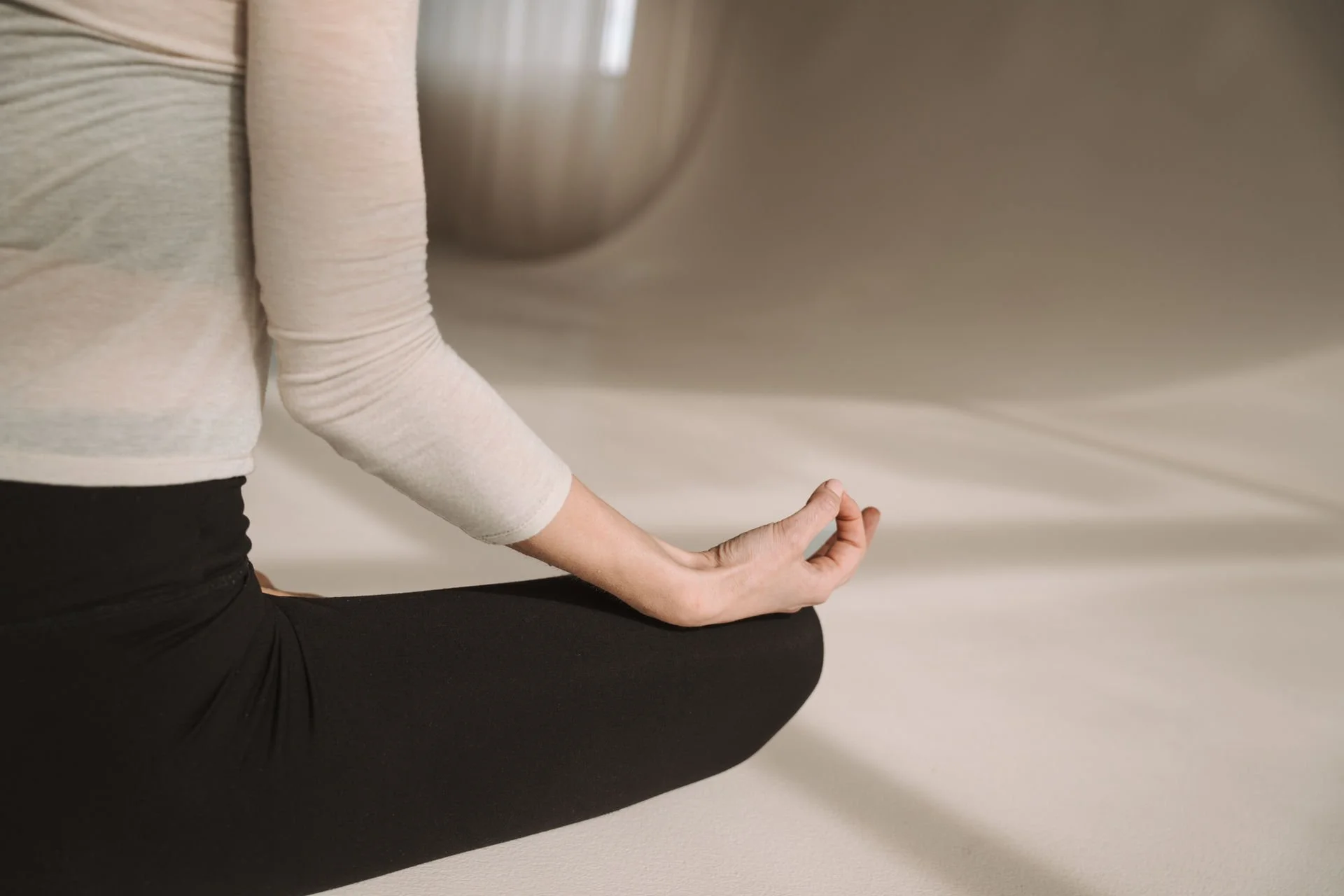 Person sitzt in der Lotus-Position auf dem Boden, Hände in Mudra-Position, in einem ruhigen Raum.