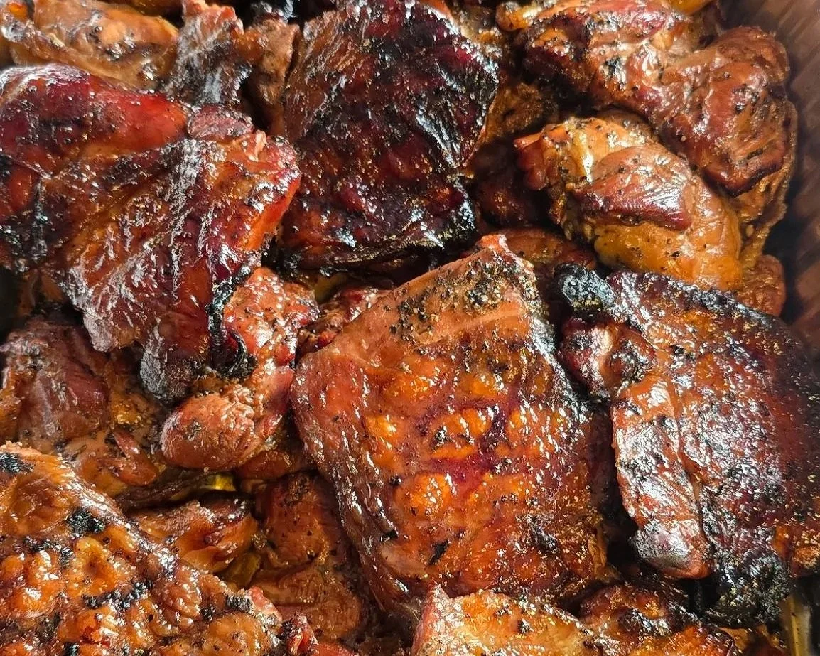 Close-up of cooked barbecue chicken thighs with a glossy, smoky glaze and charred spots.
