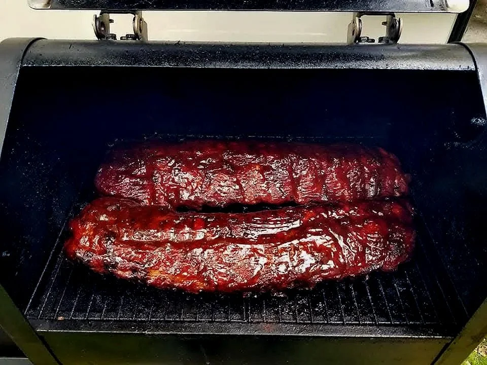 Three racks of barbecue ribs cooking on a smoker grill.