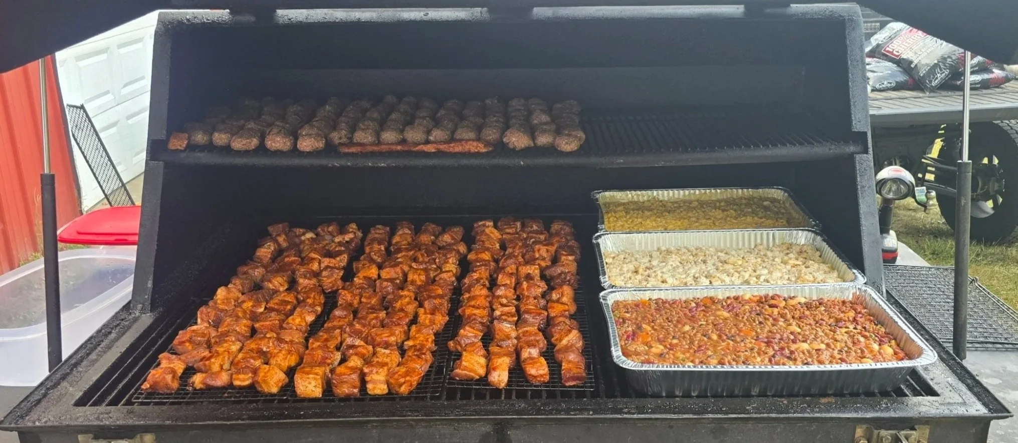 Barbecue grill with chicken wings, meatballs, cornbread casserole, and baked beans.