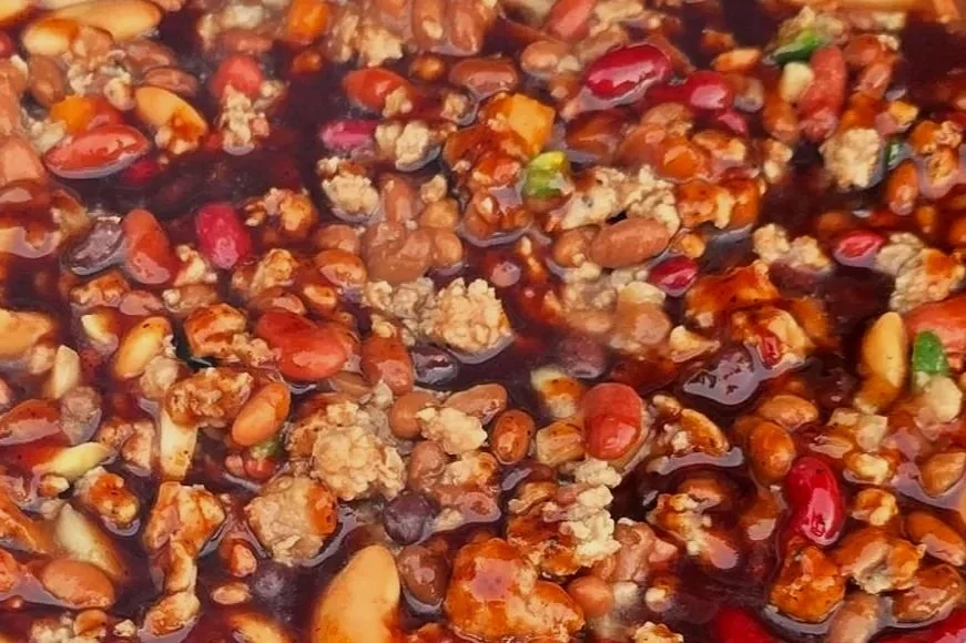 Close-up of a spicy chili sauce with ground meat, red and green peppers, and kidney beans.