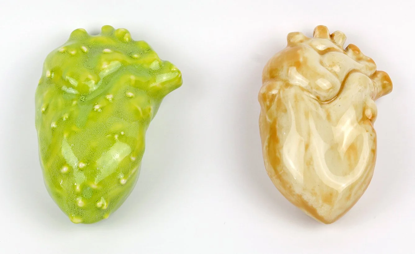 Two ceramic art sculptures resembling human hearts, one green and one beige, on a white background.