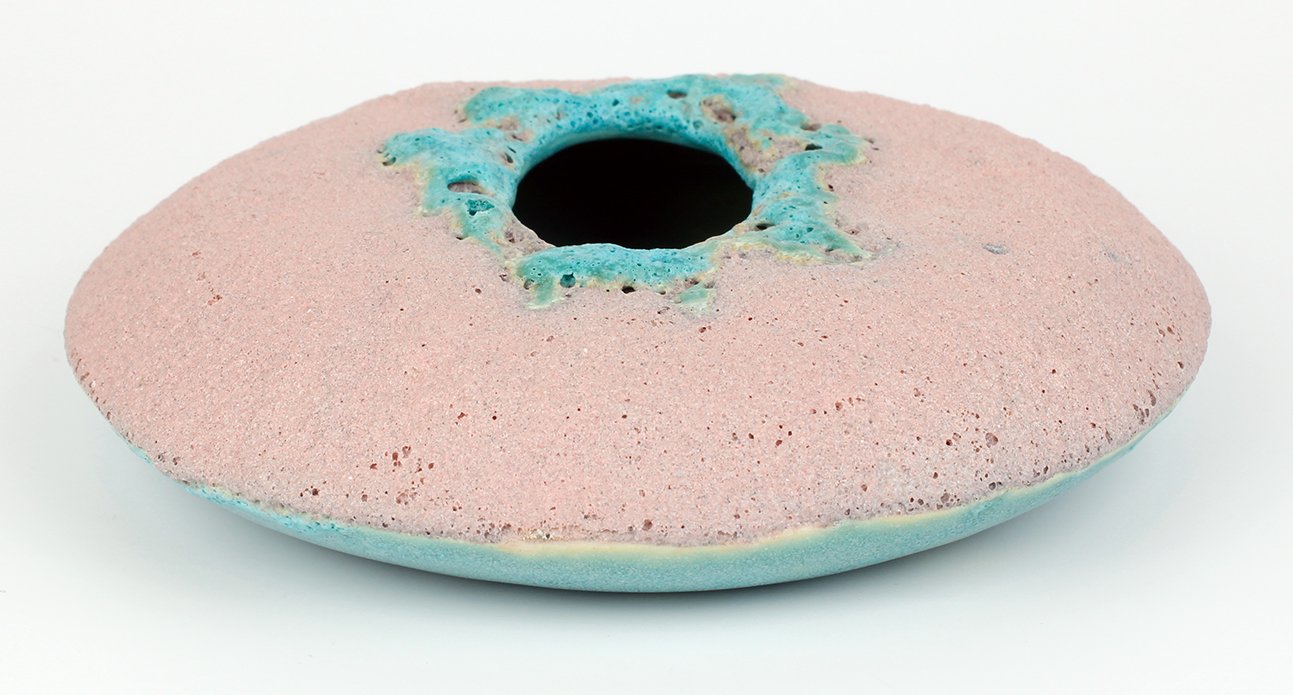 A pink and blue sponge with a hole in the center, used for cleaning or bathing.