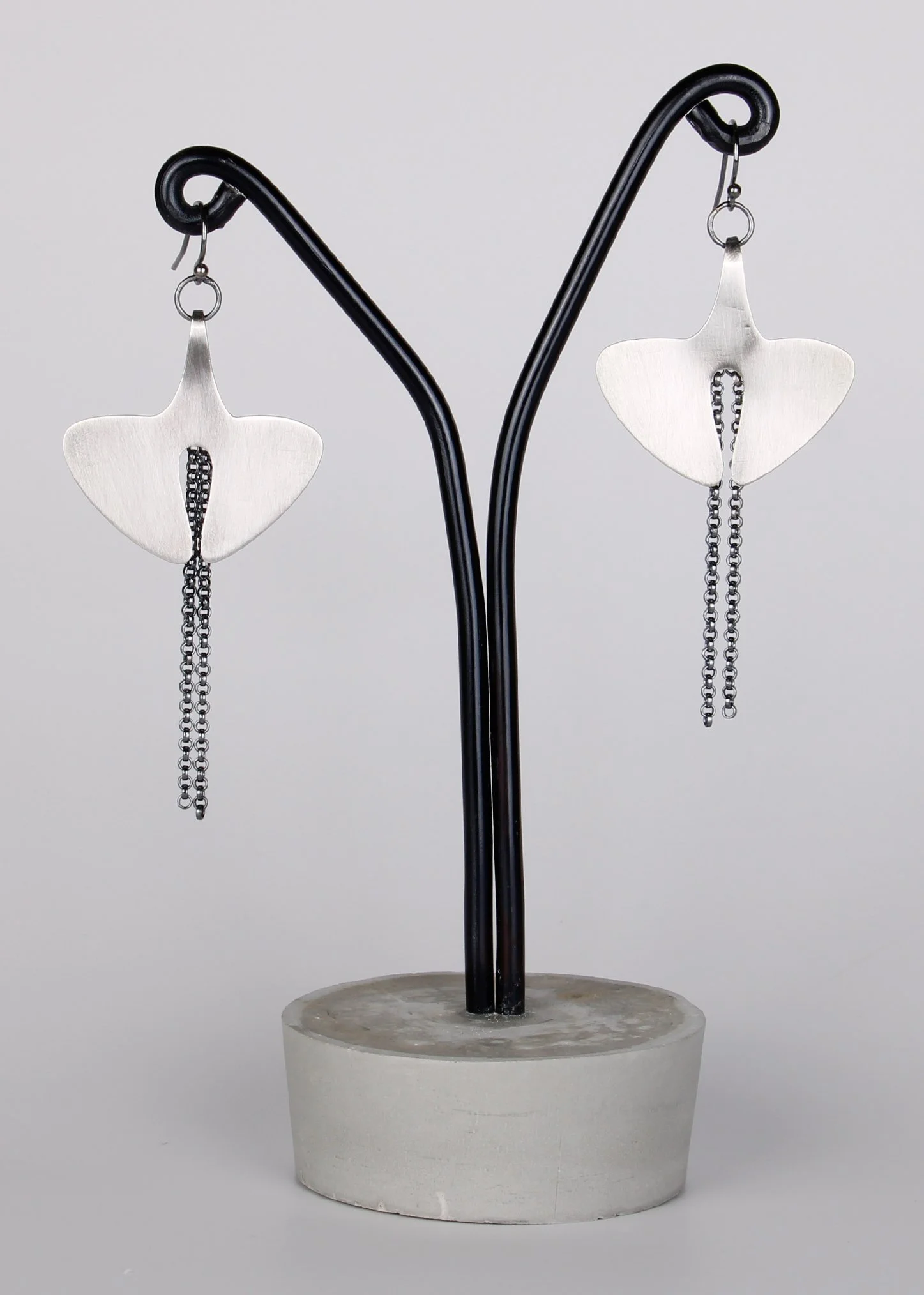 Silver earrings with butterfly-shaped tops and dangling chains on a black display stand.