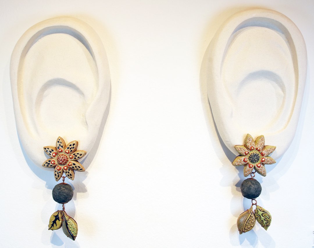 Earrings hanging on a white display, featuring flower, leaf, and round bead designs.