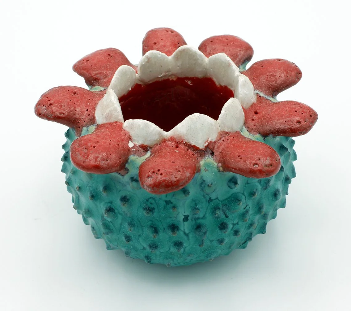 Decorative ceramic vessel resembling a strawberry with a bright blue textured surface, red petal-like ornamentation around the opening, and a white and red interior.