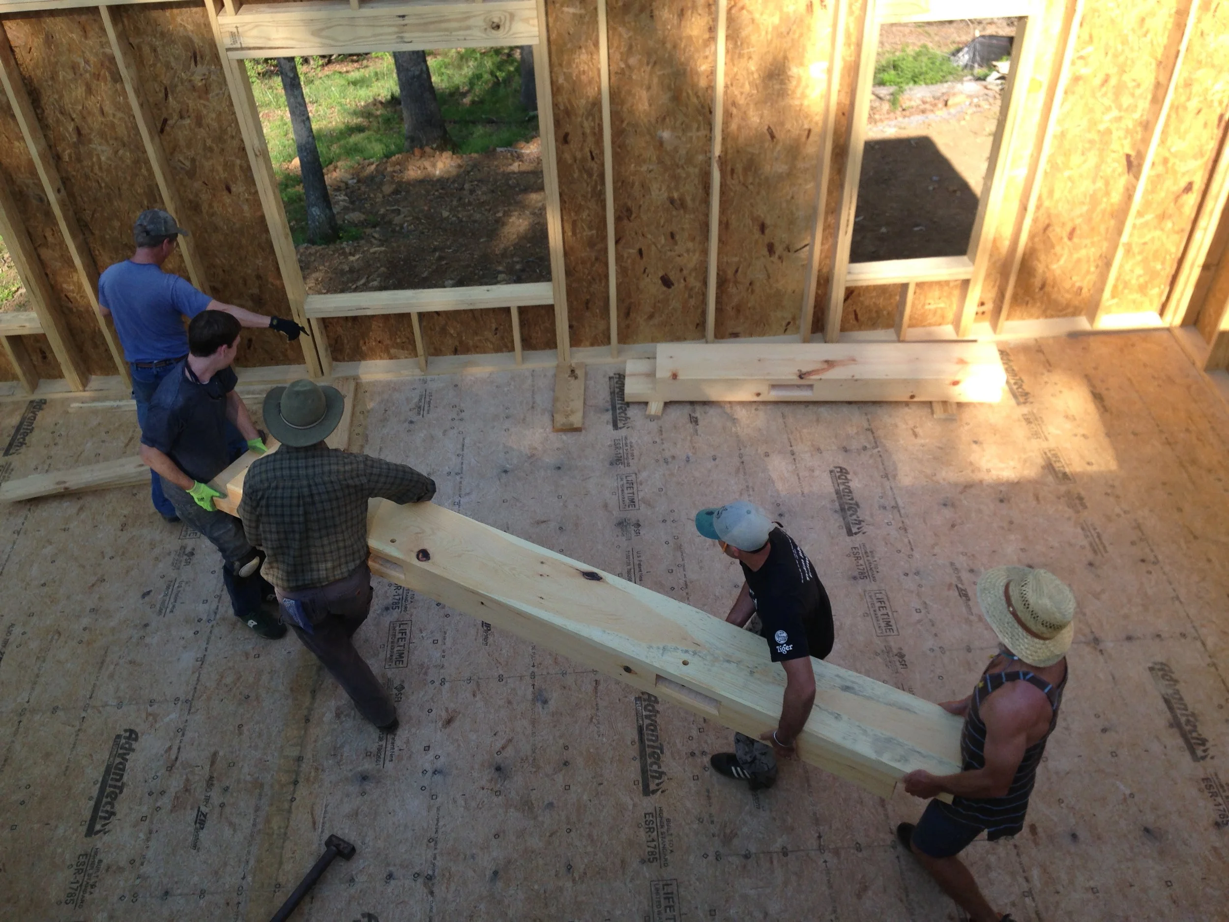 Five people working together to lift a large wooden beam inside a residential building under construction.