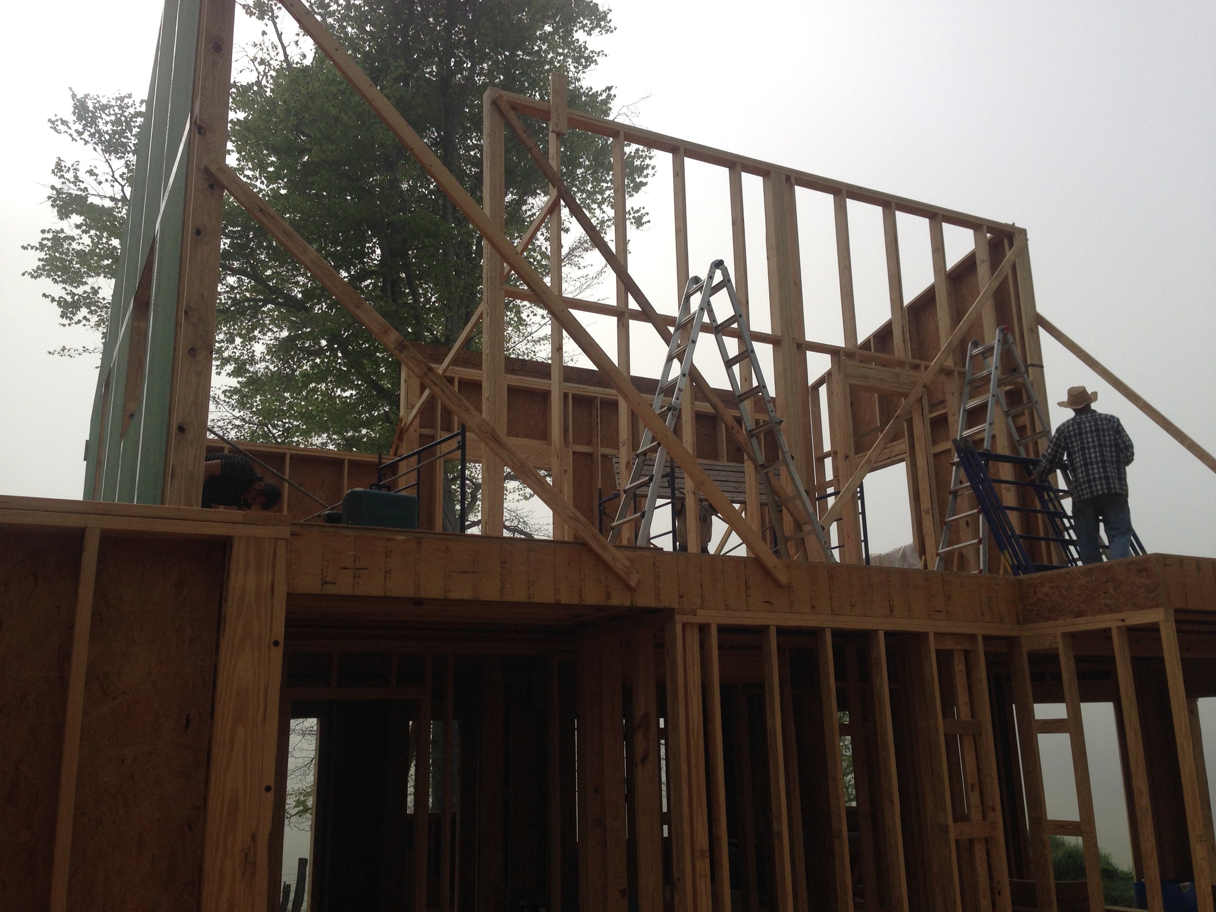 Construction workers building a wooden house frame outdoors on a cloudy day.