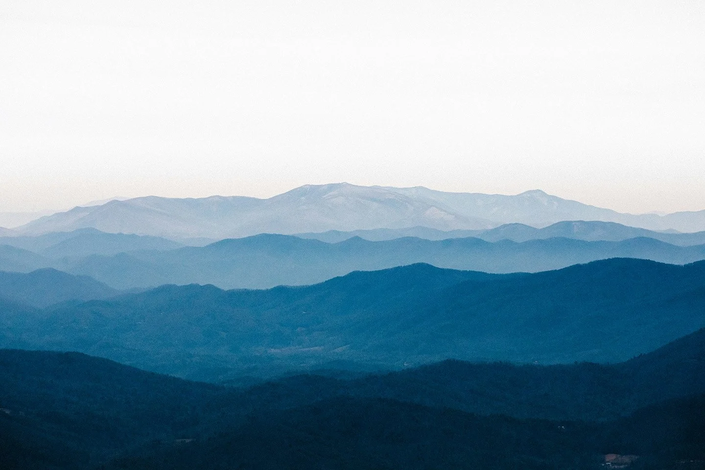 Multiple mountain ranges with a distant mountain peak at the horizon under a clear sky.