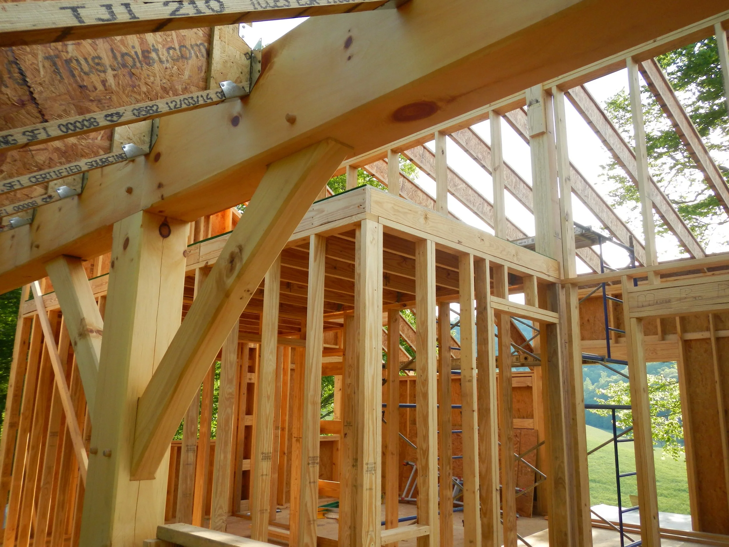 Wooden framing of a house under construction with visible beams, studs, and support braces in an outdoor setting.
