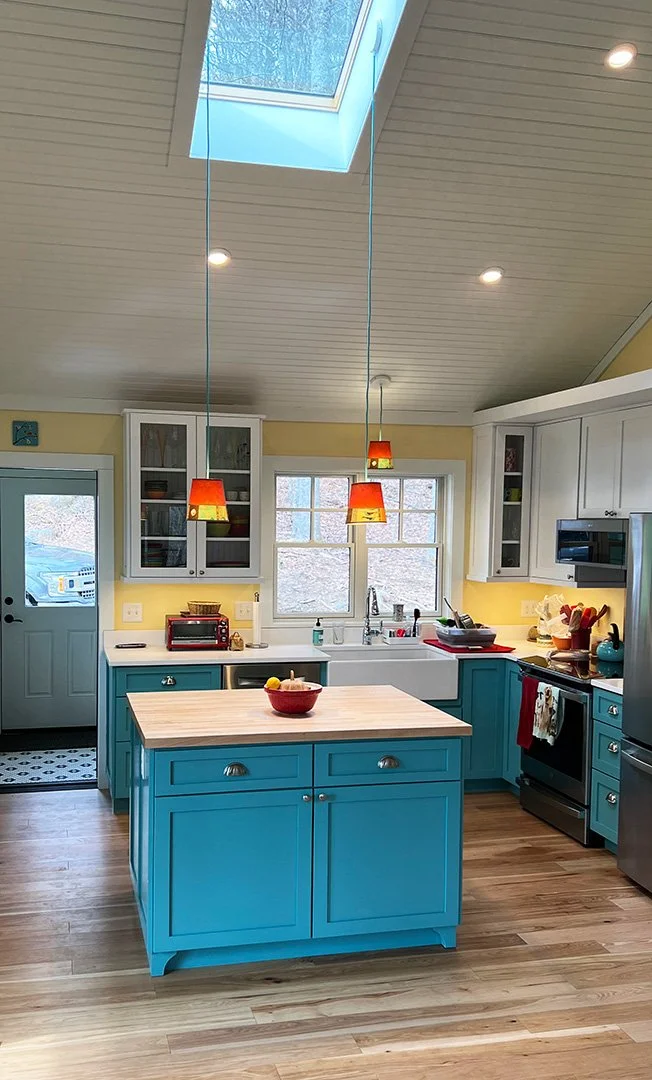 A bright kitchen with a blue island, yellow walls, white upper cabinets, and a skylight in the ceiling.