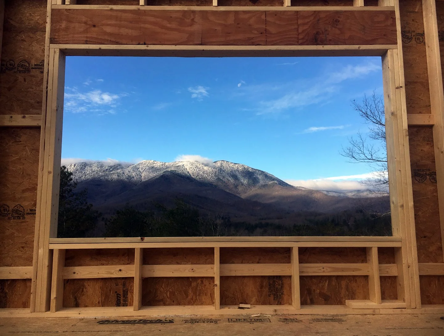 View of snow-capped mountains through an unfinished wooden structure with a large window opening.
