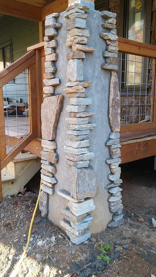 A concrete pillar with natural stone pieces glued around its edges, part of a deck's staircase support.