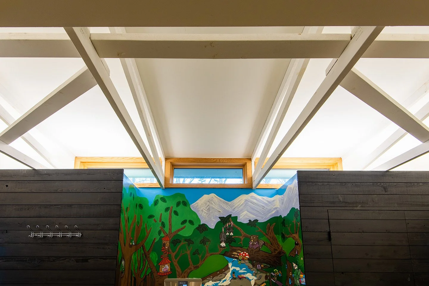 Colorful mural of a forest scene with trees, mountains, animals, and nature elements on a wall inside a building.